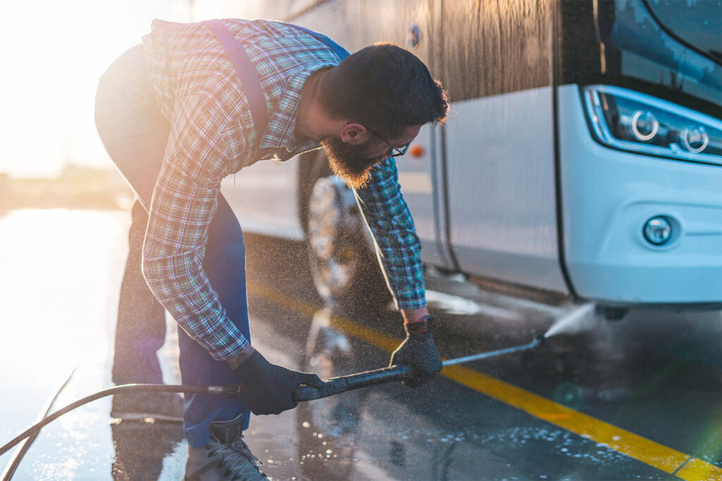 a staff member cleaning the underbody of a bus with a jet pressure washer