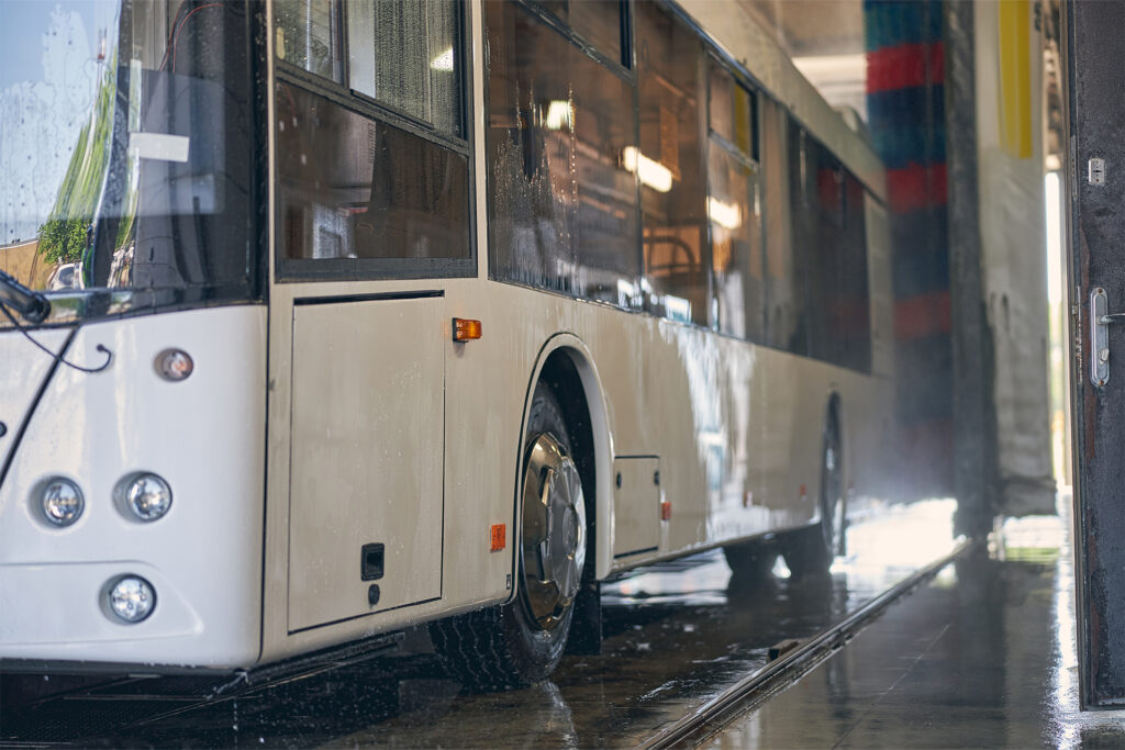 a white coach in a drive through bus wash system covered in water